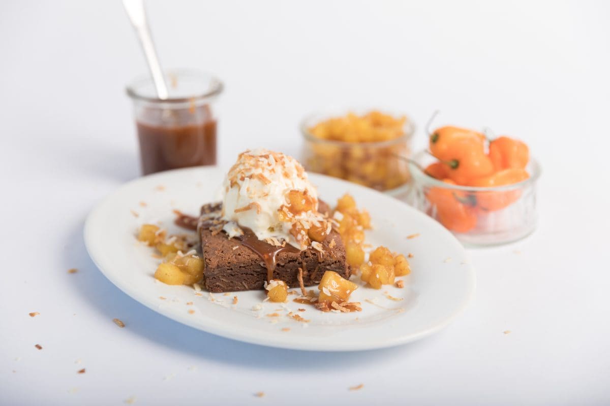 Plated Coconut Habanero Brownie topped with Habanero Peppers, Pineapple, and Caramel Sauce.