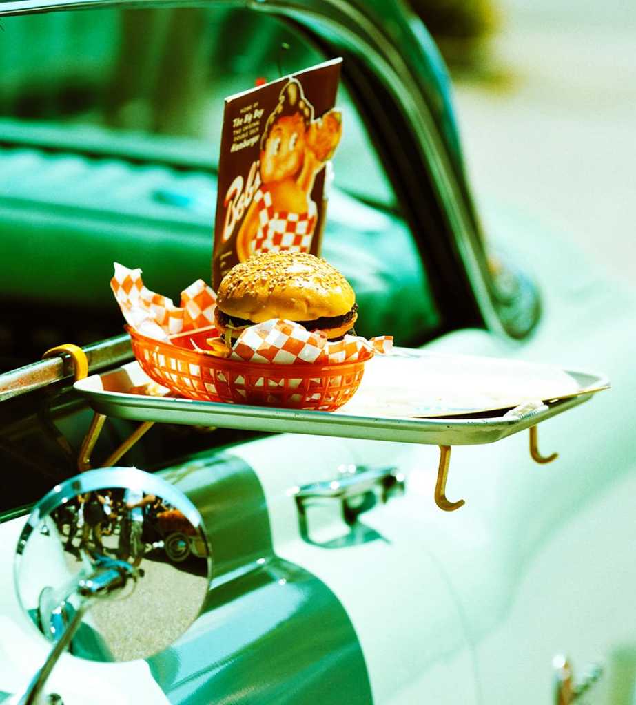 Old fashioned curb-side service from a car hop, bringing a basket containing a hamburgers and fries.