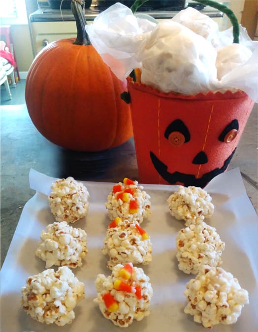 Halloween popcorn balls on a tray, garnished with candy corn, sitting in front of a jack-o-lantern trick-or-treat bag.