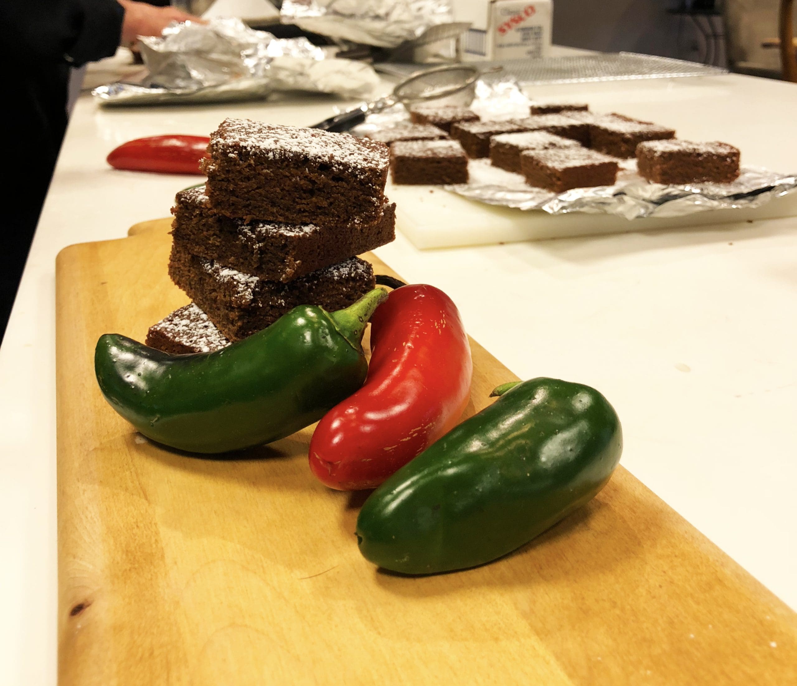 A stack of chocolate brownies on a cutting board next to fresh red and green jalapeno peppers.